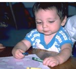 [photo of young male child drawing with crayons.]